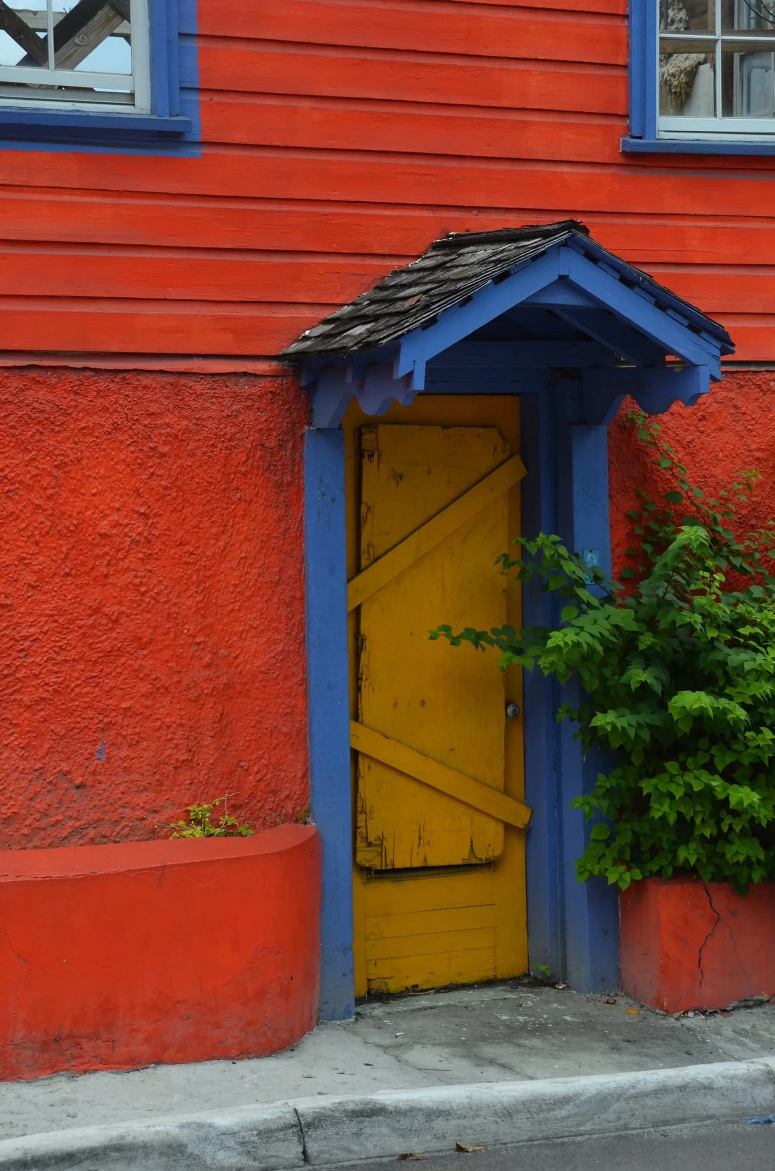 Yellow wooden door under a small blue porch roof in a red wall in Nassau